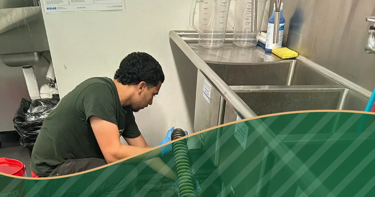 Worker handling a vacuum hose beside a stainless steel commercial kitchen sink