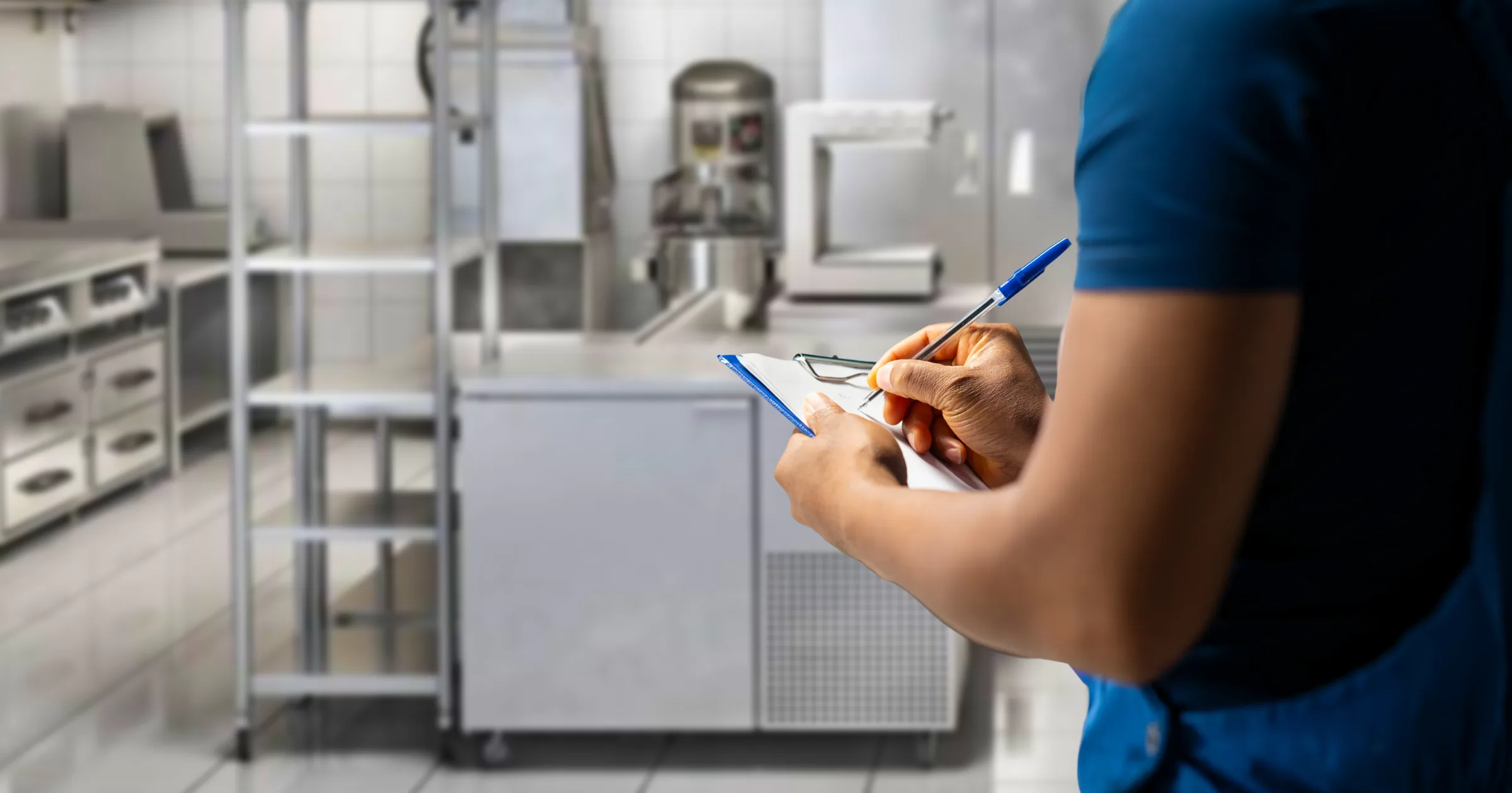 Inspector writing on a clipboard in a stainless steel commercial kitchen
