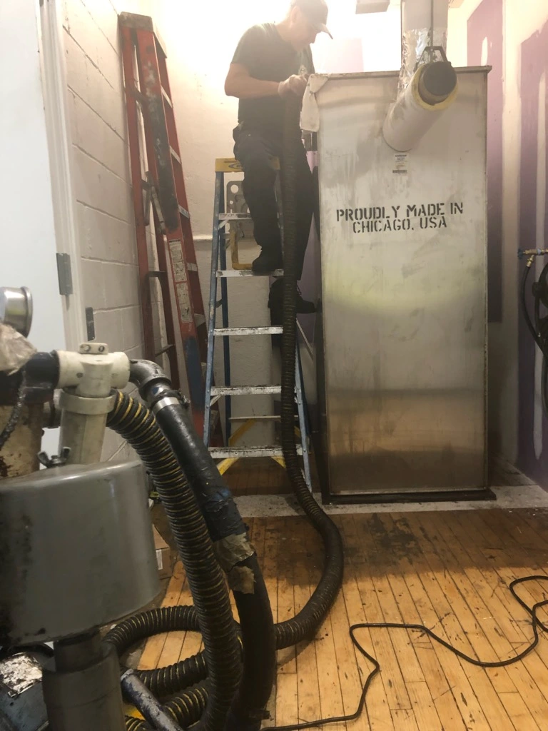 A&L worker on a ladder feeding a vacuum hose into a tall stainless tank