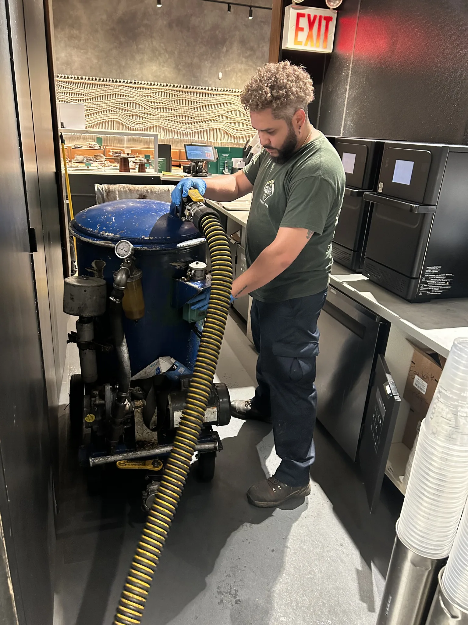 A&L technician running a portable blue vacuum machine, hose in hand, in a café service line