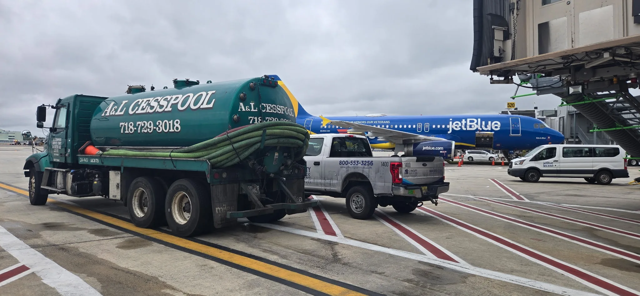 A&L Cesspool vacuum tanker on an airport apron with a JetBlue aircraft at the gate behind it