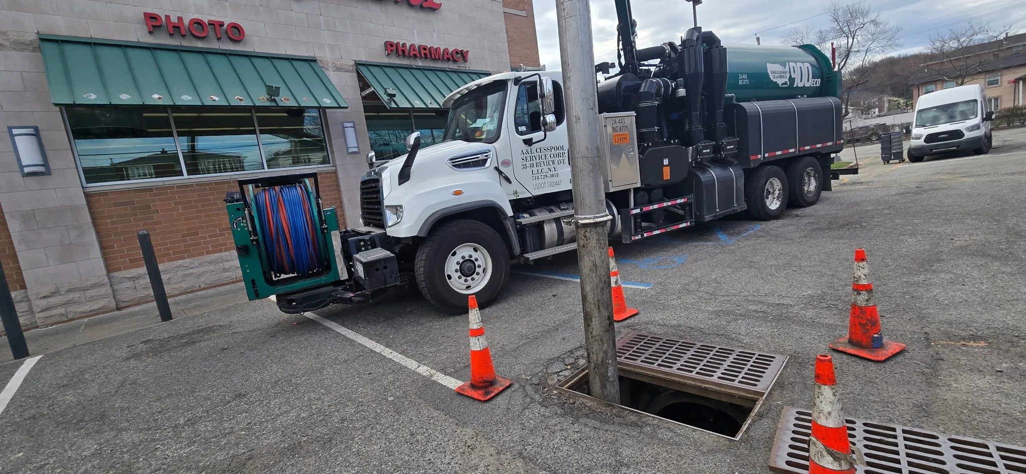 A&L JetVac truck at an open catch basin in a pharmacy parking lot with cones set out