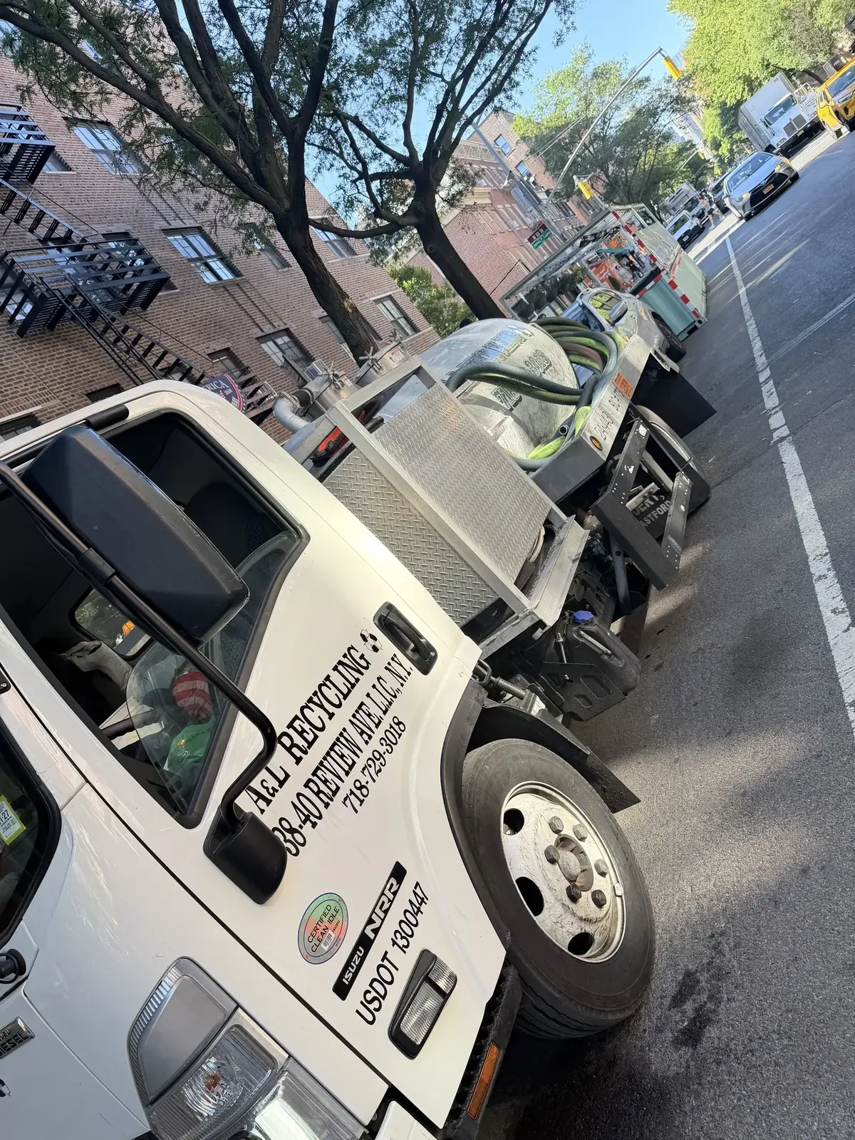 The Silver Bullet, A&L's compact white truck with a stainless tank, parked on a tree-lined New York street with the hose coiled