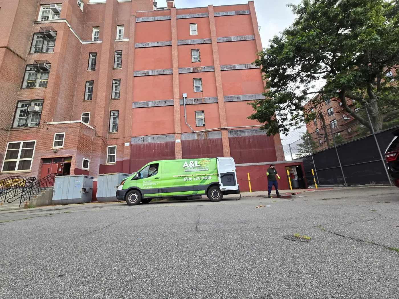 Green A&L jetting van parked at a large brick apartment building on a New York street