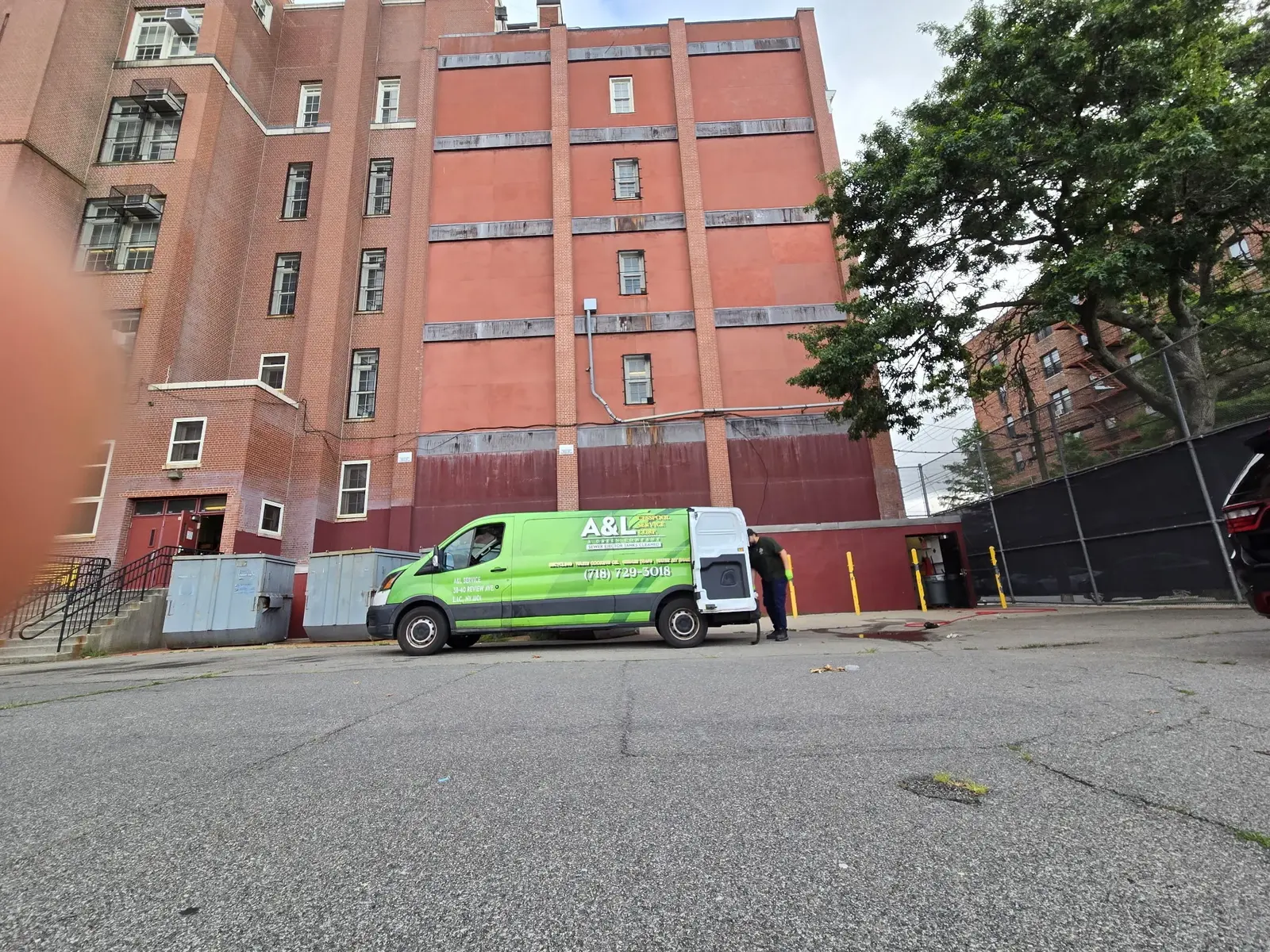 Bright green A&L service van with its rear doors open at a large brick apartment building