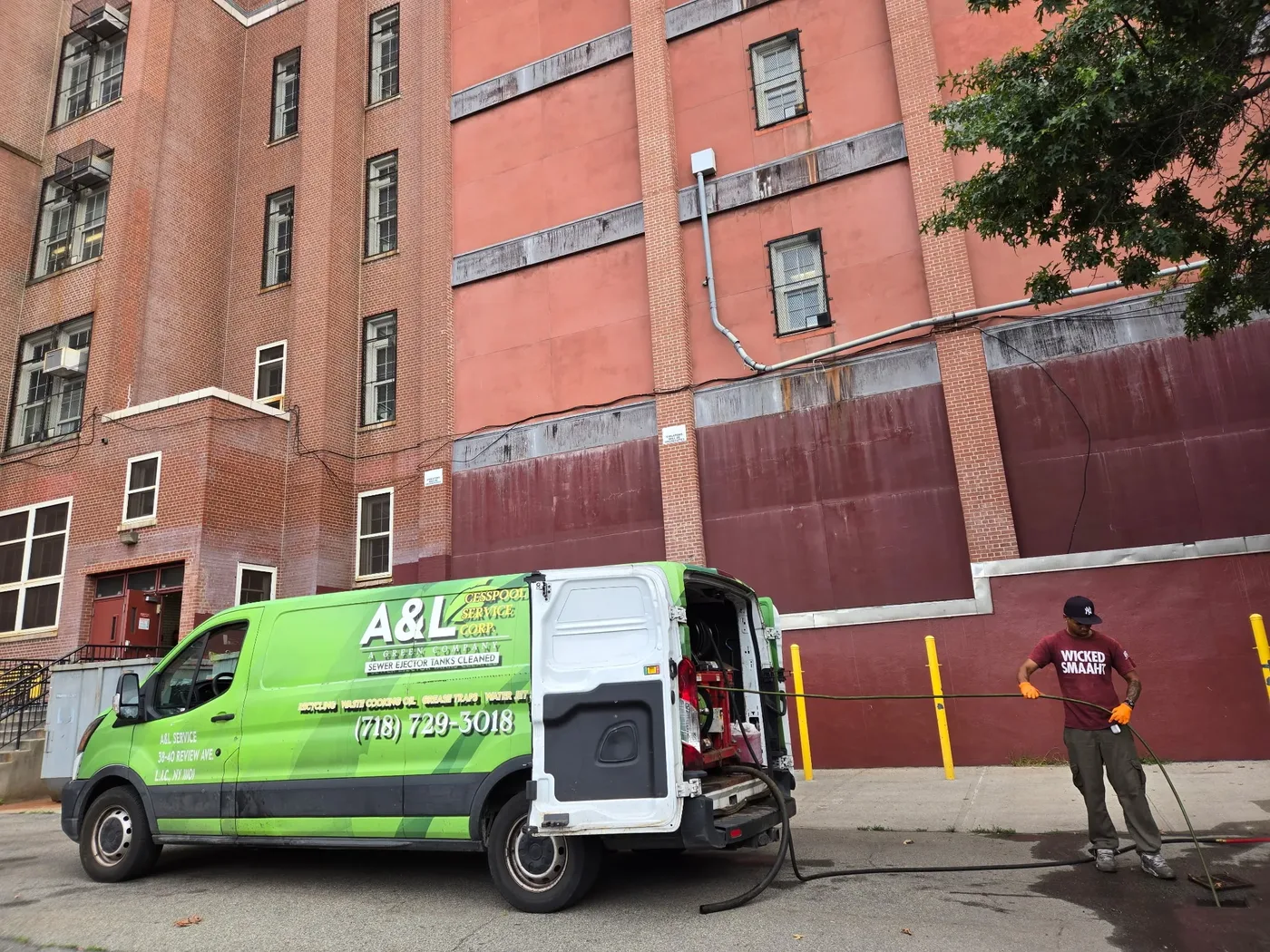 A&L technician running a sewer ejector line from the green jetting van at a brick apartment building