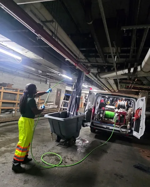 A&L technician Trent Paul running a green water jet hose beside an open van jet inside a building